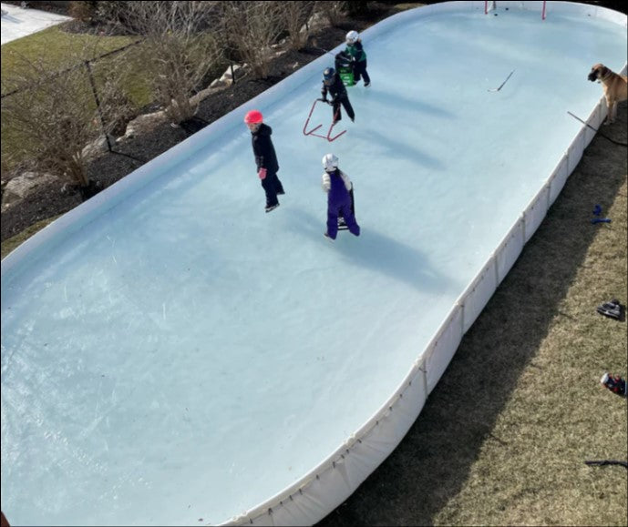 Four kids on a large backyard ice hockey rink with a net 