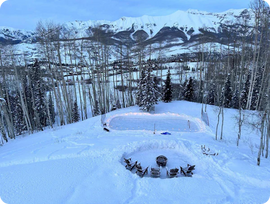 A backyard ice rink on a very snowy day next to five chairs and a fire pit