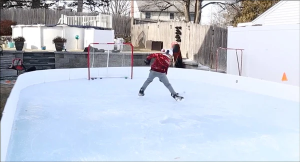 A kid about to shoot a hockey puck into a net on a backyard ice rink.