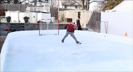 A kid about to shoot a hockey puck into a net on a backyard ice rink.