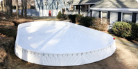 An empty YardRink backyard ice rink kit fully assembled with its white panel and white liner, installed on a lawn next to a residential house before being filled with water.